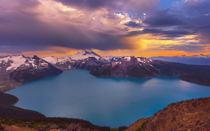 Turquoise lake surrounded by snow-capped mountains under a dramatic sky