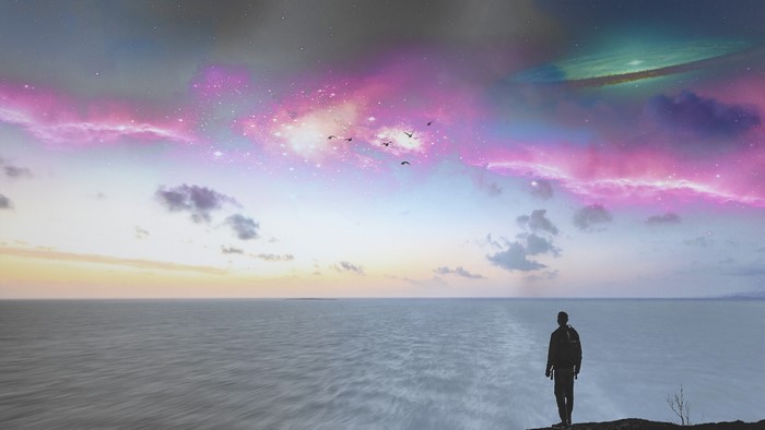 Man looking at colorful galaxy sky over ocean