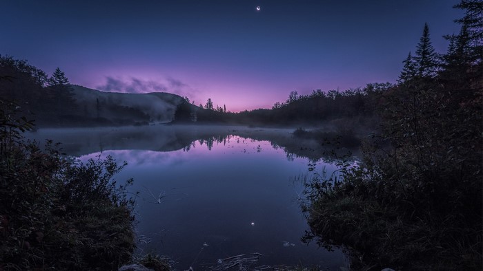 Misty lake at night with moon and purple sky
