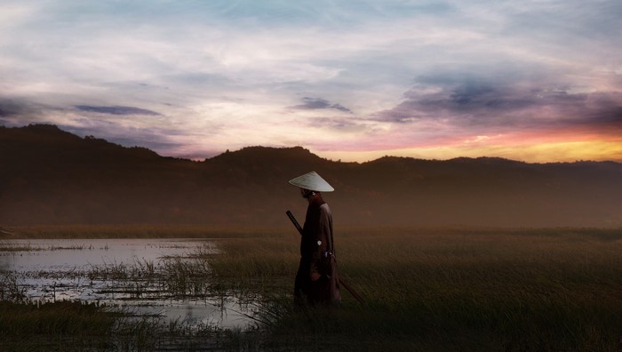 Samurai warrior with sword at sunset near mountains