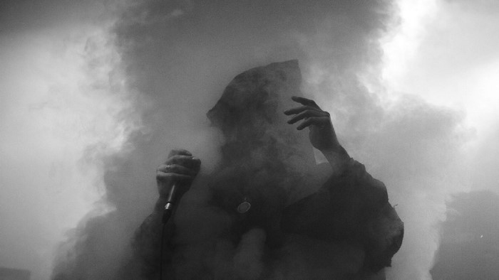 Man in hood holding microphone in smoke