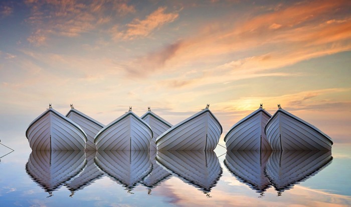 Several white boats floating on calm water with sunset sky reflection