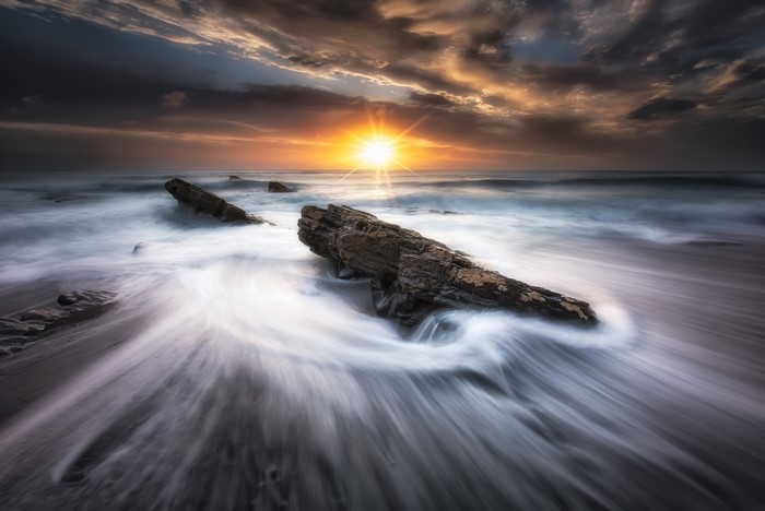 Sunset over the ocean with rocks and waves