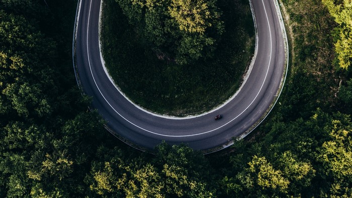 Aerial view of a winding road through a forest with a motorcycle
