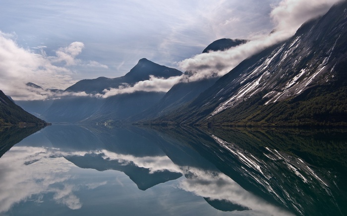 Mountains reflected in a calm lake under a cloudy sky