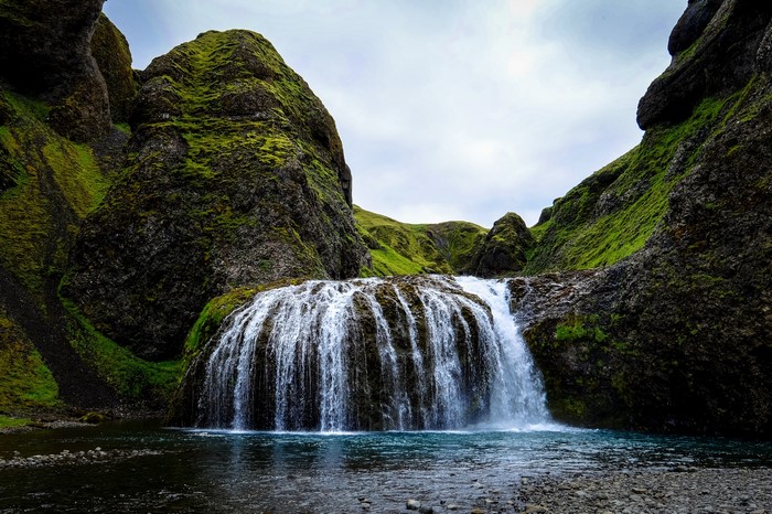 Mossy cliffs surround a wide waterfall into a pool