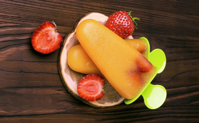 Orange popsicles with strawberries on a wooden surface