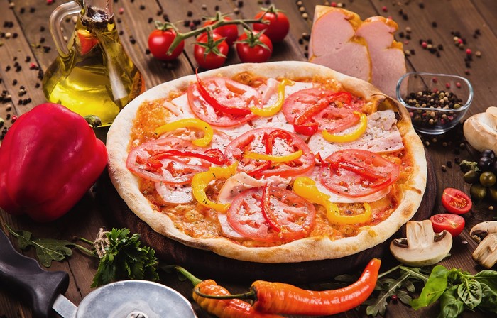 Pizza with tomatoes, bell peppers, and ham on a wooden surface