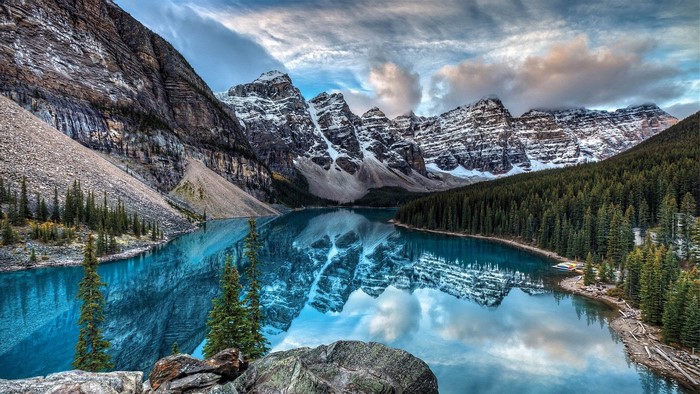 Turquoise lake reflecting snow-capped mountains and pine forest