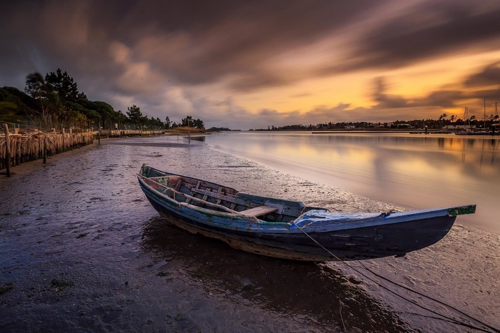 Boat on a muddy shore at sunset with long exposure clouds