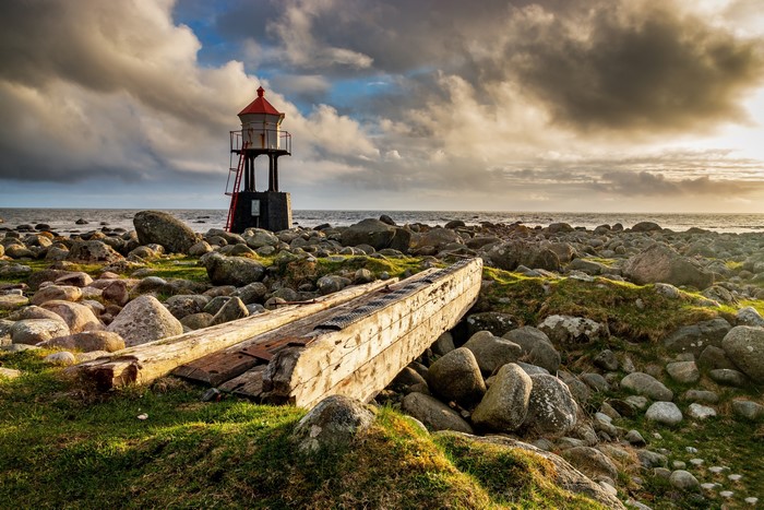 Lighthouse on a rocky coast with a shipwrecked boat