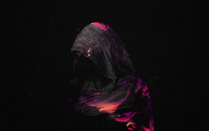 Hooded figure with colorful particles against black background