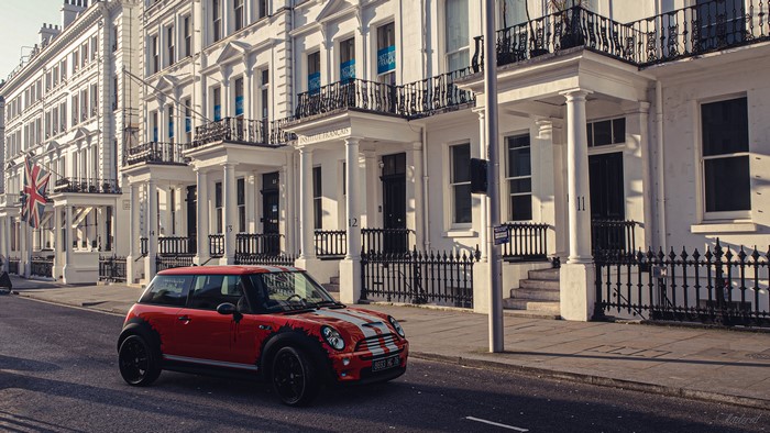 Red Mini Cooper parked in front of white buildings in the UK