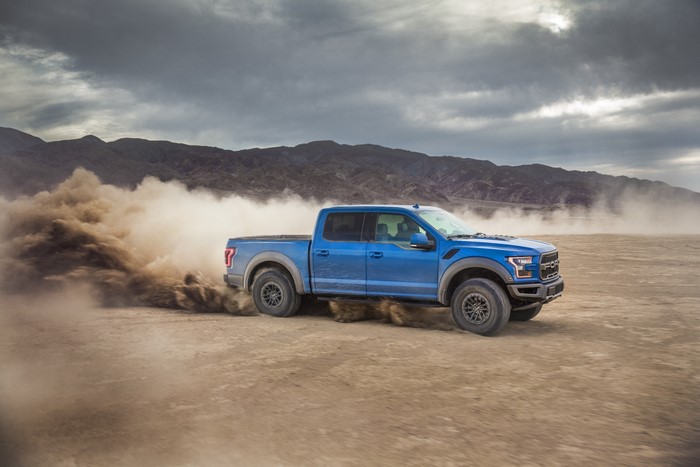 Blue Ford F-150 Raptor driving through dust in desert