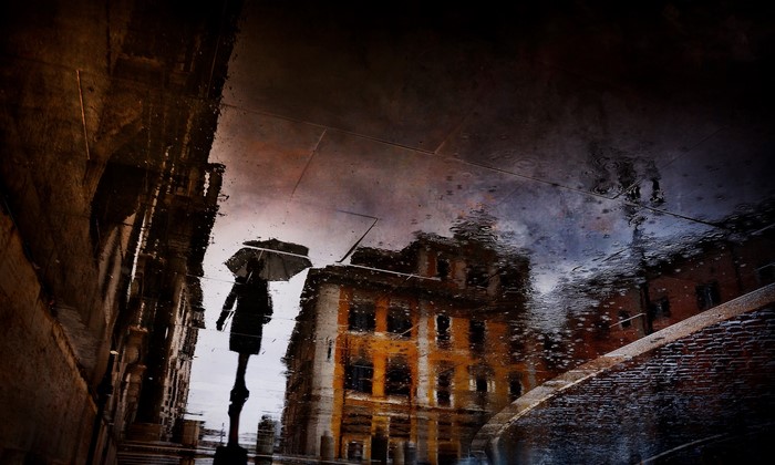 Reflection of a person with an umbrella in a rainy city