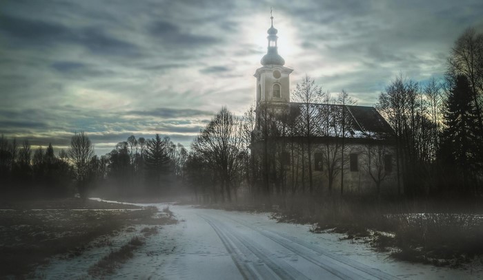 Winter church on a snowy road with dramatic sky