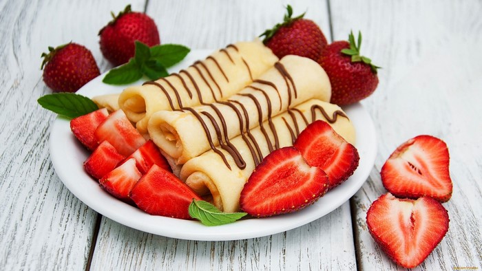 Rolled crepes with chocolate drizzle and strawberries on a plate