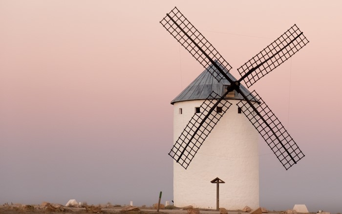 White windmill with black sails against pink sky
