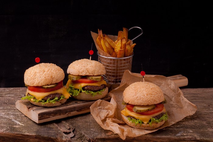 Three burgers and fries on a wooden table