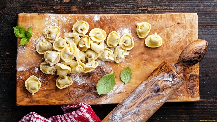 Fresh tortellini and basil on a wooden cutting board