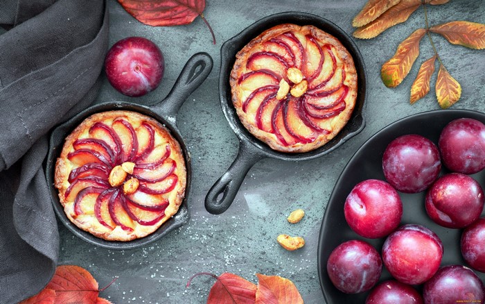 Plum tarts in cast iron pans with plums and autumn leaves
