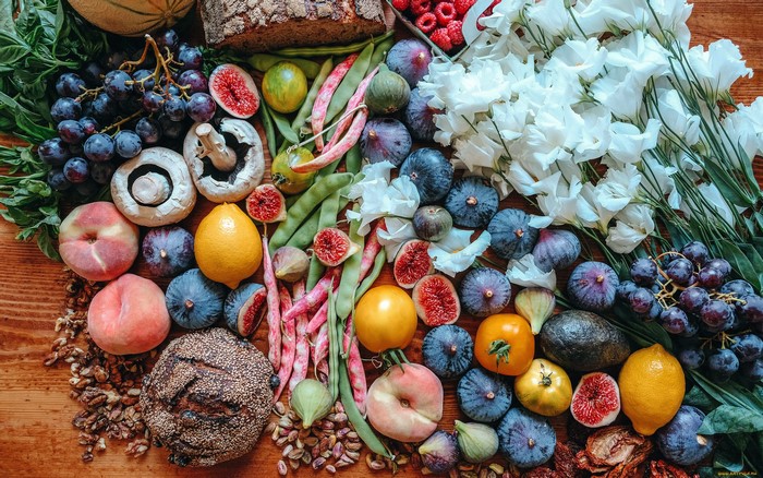 Assortment of fresh fruits, vegetables, bread, and flowers on a wooden surface
