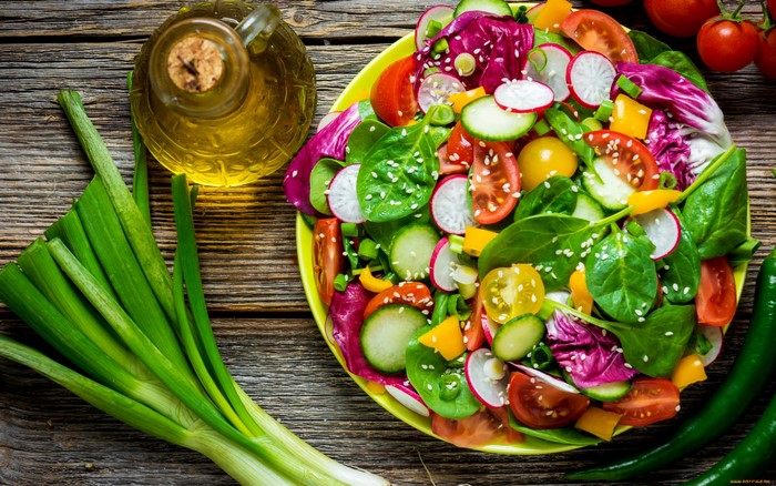 Fresh salad with vegetables and olive oil on a wooden surface