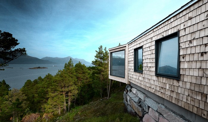 Modern wooden house with large windows overlooking a lake and mountains