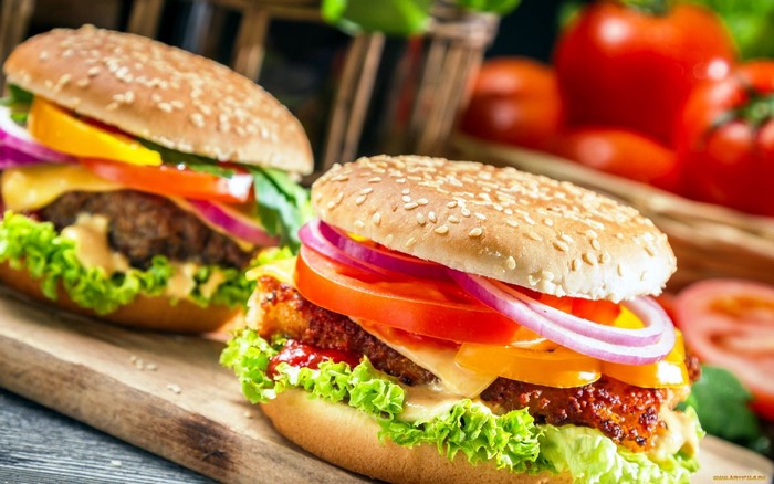 Two gourmet burgers on a wooden board with tomatoes