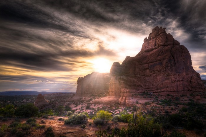 Sunlight breaking through clouds over rock formation in Arches National Park