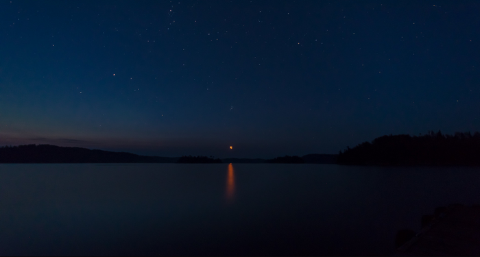 Night sky over a lake with stars and moon reflection