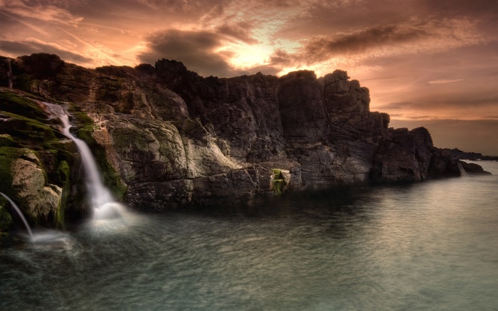 Waterfall cascading over rocks into the sea at sunset