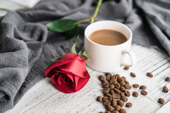 Coffee cup with rose and coffee beans on planks
