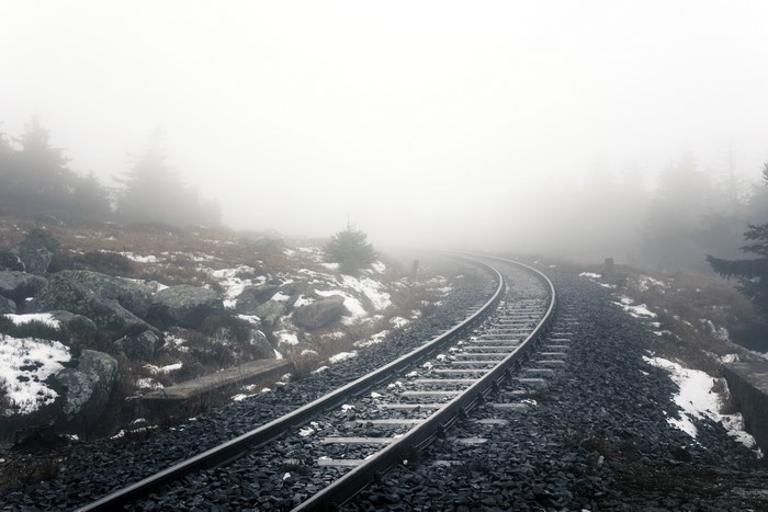 Railroad track curving through a foggy, rocky landscape
