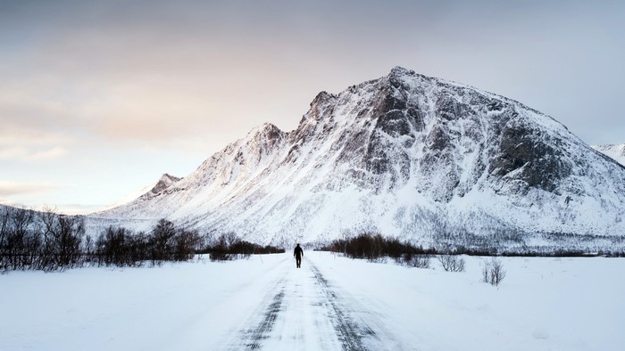 Man walking on snowy road towards mountains in winter