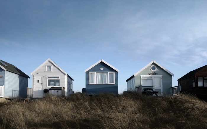 Beach huts lined up on a grassy dune under a blue sky