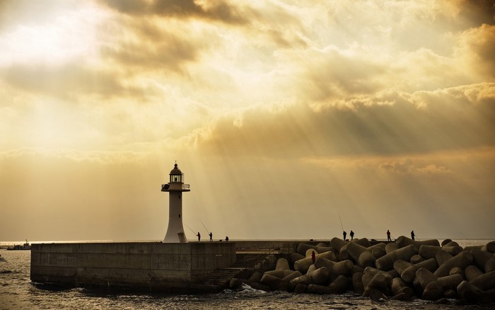Lighthouse on a breakwater with fishermen at sunset