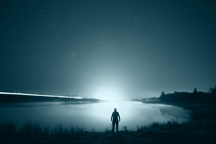 Man standing by a lake under a starry night sky