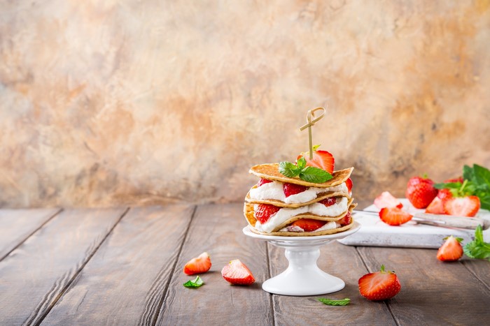 Stack of pancakes with strawberries and cream on a cake stand