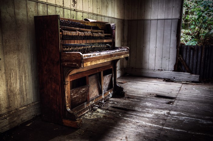 Abandoned upright piano in a derelict room