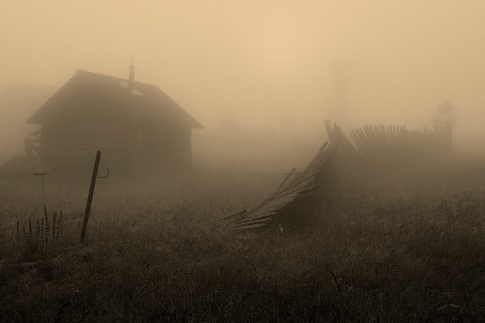 Abandoned cabin in the mist with a broken fence