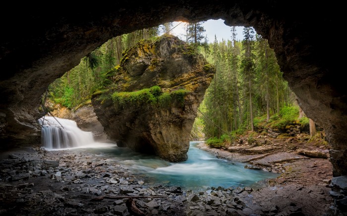 Cave entrance overlooking a waterfall and river in a forest