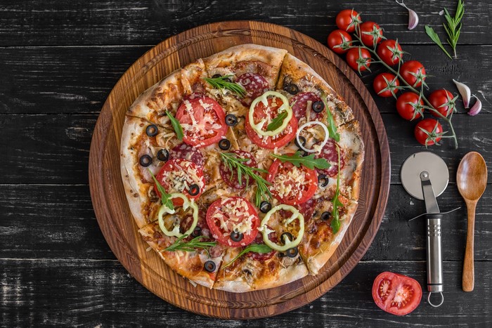 Pizza with tomatoes, olives, and salami on a wooden board