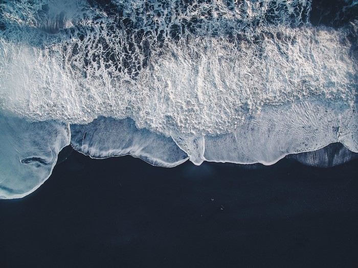 Aerial view of waves crashing on a black sand beach