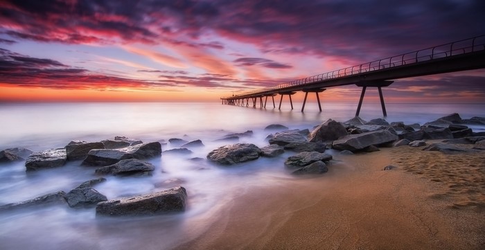 Pier over the sea at sunset with colorful sky and rocks
