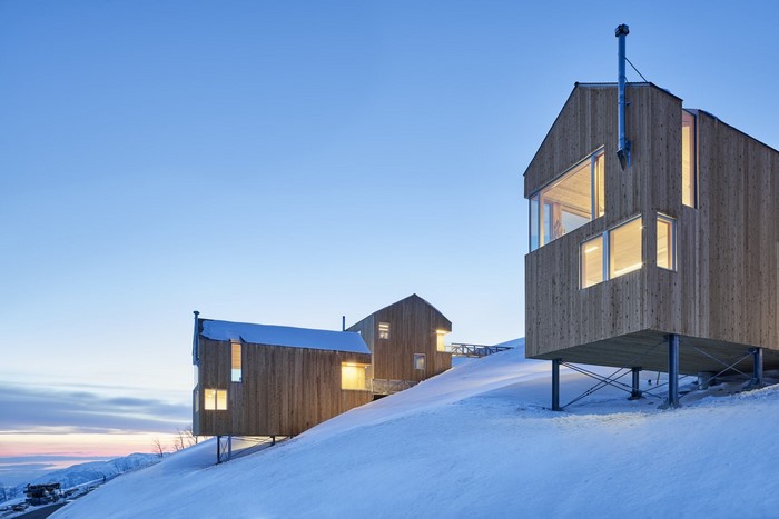 Modern wooden cabins on a snowy slope at dusk