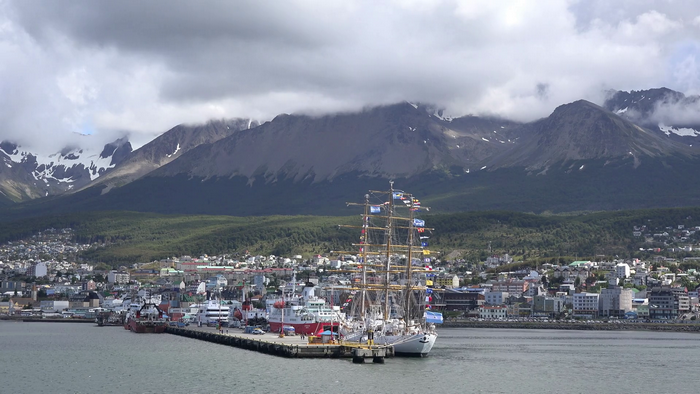 Tall ship docked in Ushuaia harbor with mountains in background