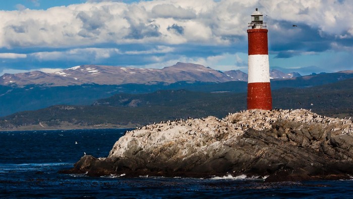 Red and white lighthouse on a rocky island with penguins
