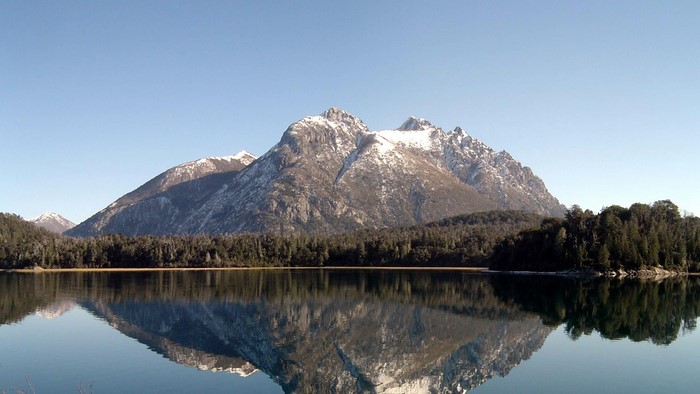 Snow-capped mountains reflected in a lake with pine forest