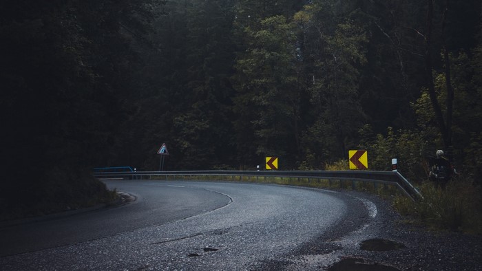 Curving mountain road with warning signs and trees